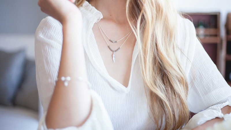 Woman in a white blouse wearing layered fine necklaces and a pearl bracelet.