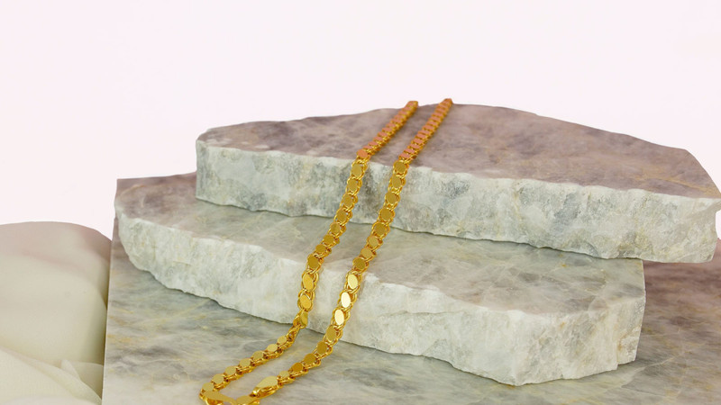 Gold link chain draped over pale marble slabs on a white background.