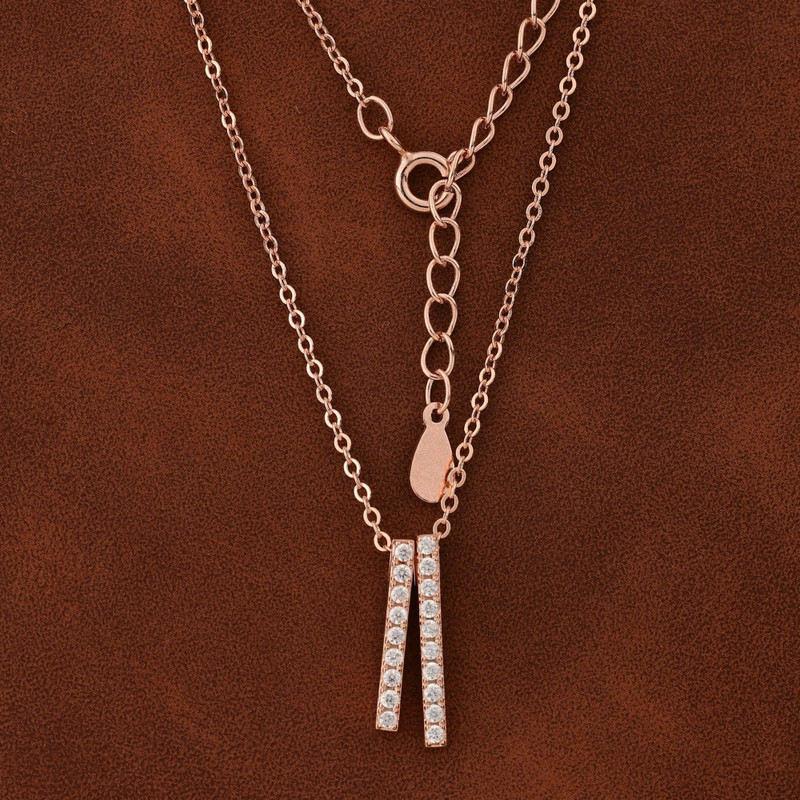 Two rose-gold chains with twin pavé bar pendants on warm brown leather.