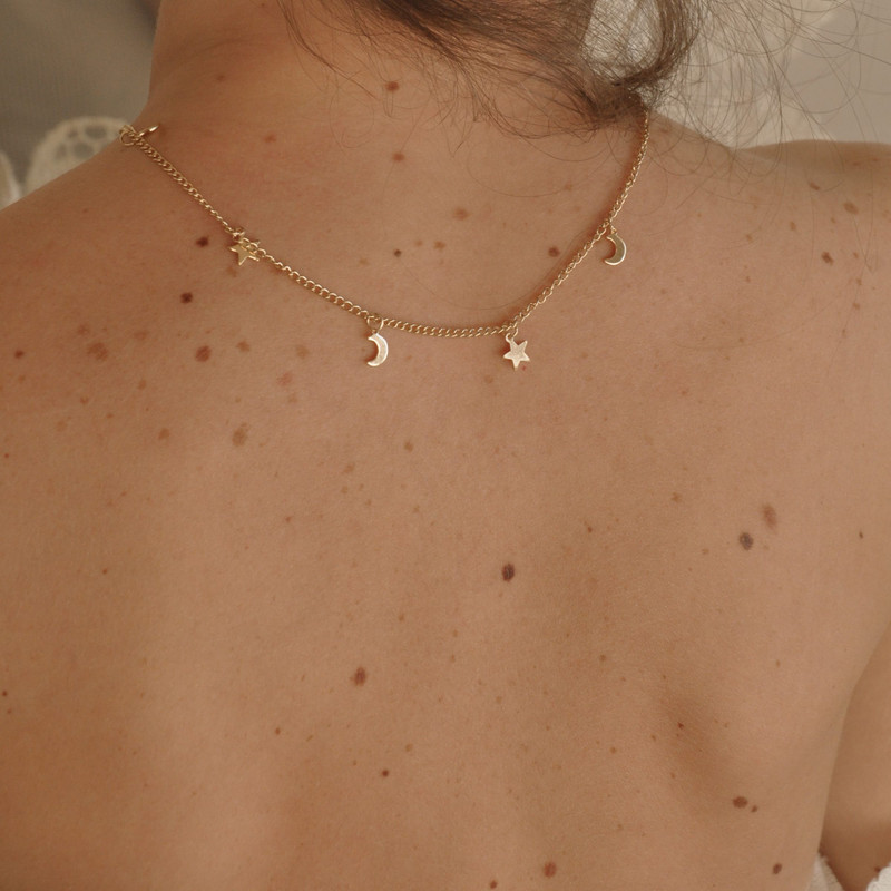 Back of the neck wearing a fine gold chain with tiny star and moon charms, warm skin.