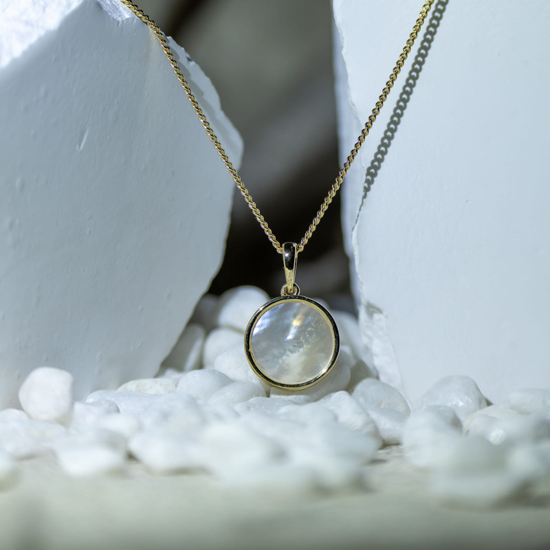 The same moonstone pendant hanging between white stones with white pebbles.