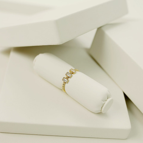 Slim gold band set with a row of baguette stones on a white roll, white studio blocks.