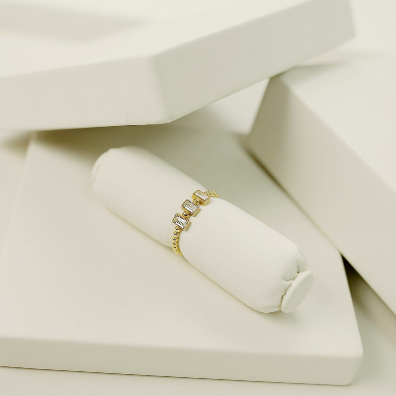 Slim gold band set with a row of baguette stones on a white roll, white studio blocks.