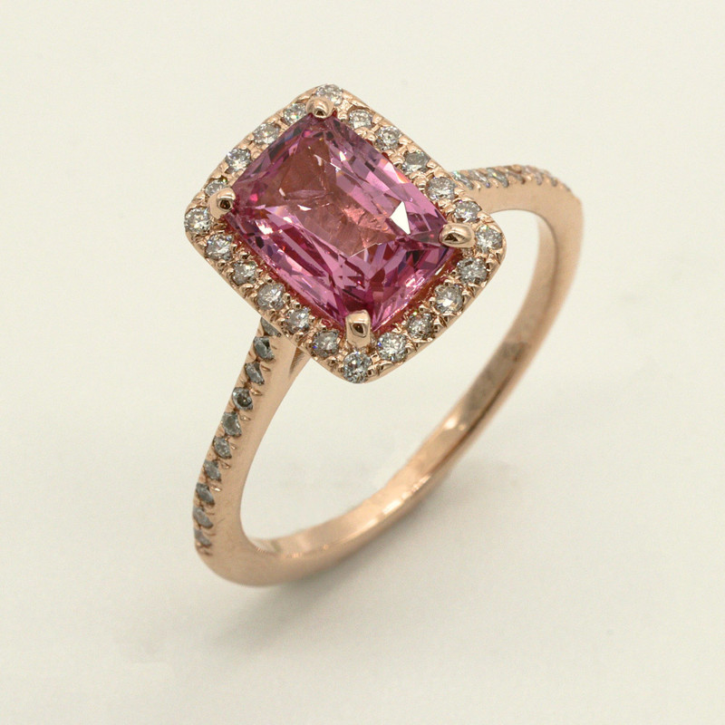 Rose-gold ring with a cushion pink stone in a diamond halo, angled on white.