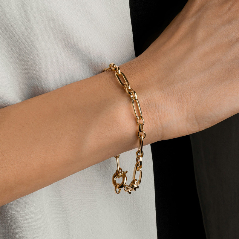 Wrist wearing a gold paperclip-link bracelet with a lobster clasp, white top.