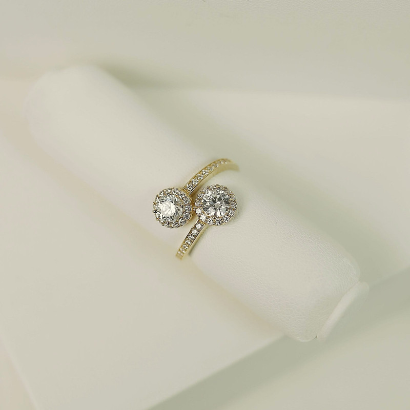 Gold toi-et-moi ring with two halo-set diamonds resting on a white roll, white studio blocks.