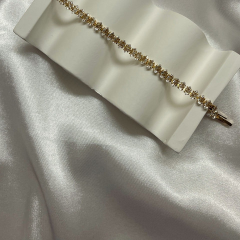 Gold tennis bracelet of small round stones laid over a white wave stand on satin.