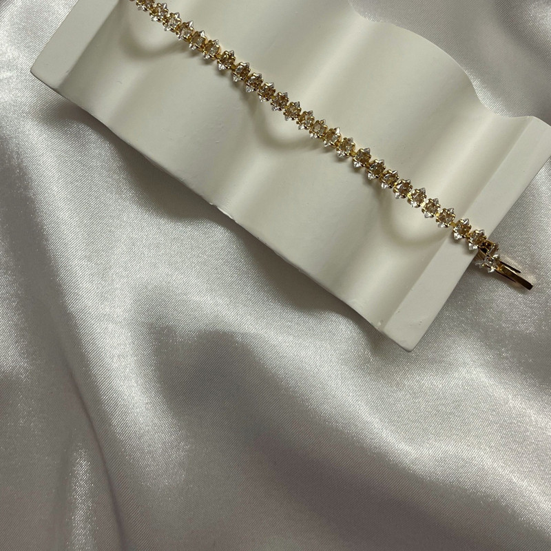 Gold tennis bracelet of small round stones laid over a white wave stand on satin.