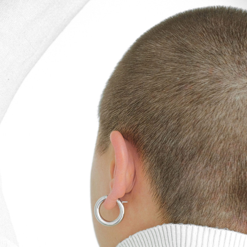 Back view of a person in a white turtleneck wearing a silver hoop, bright white background.