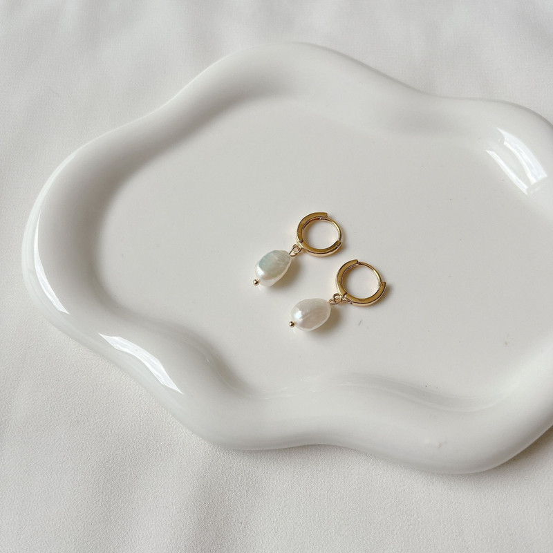 Small gold huggies with pearl drops on a white wavy ceramic dish.