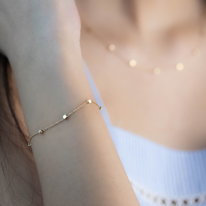 Fine gold chain bracelet with tiny stations on a wrist, soft neutral light.
