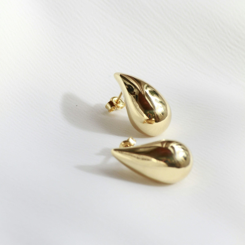 Second angle of the same gold teardrop earrings on white.