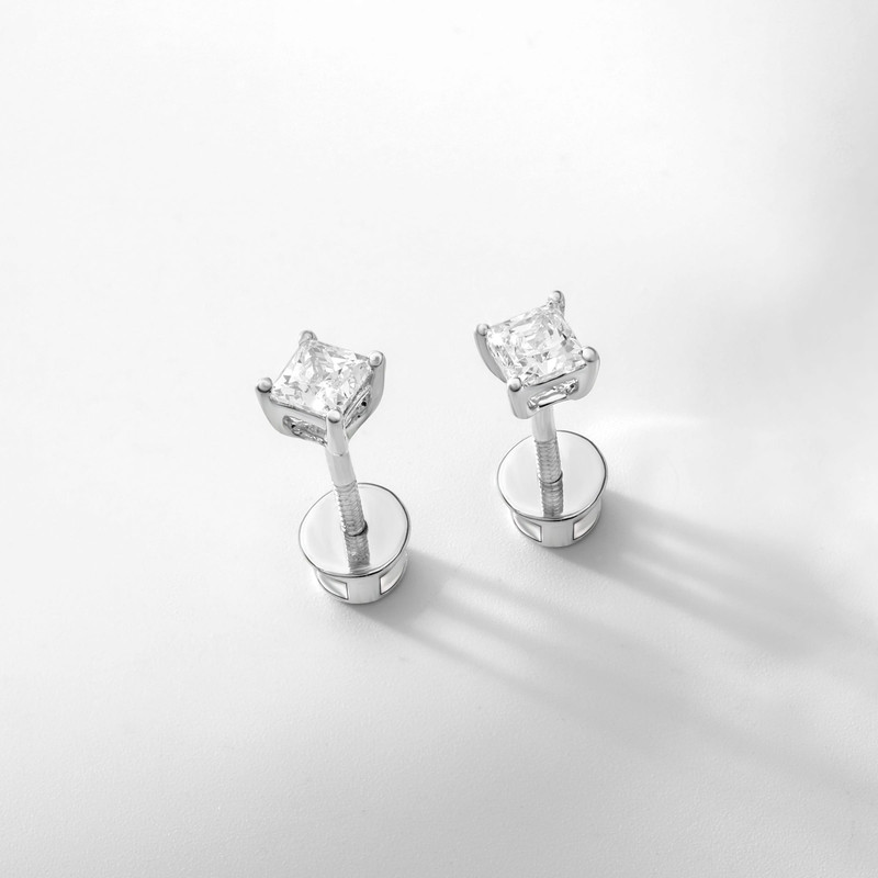 Princess-cut diamond studs in white metal with long soft shadows on white.