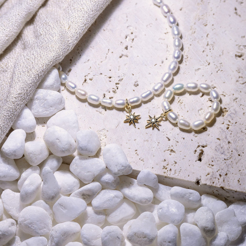 Freshwater pearl necklace with small gold star charms on travertine with white pebbles.