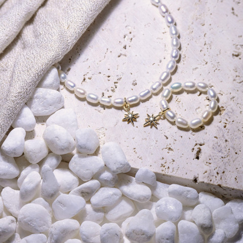 Freshwater pearl necklace with small gold star charms on travertine with white pebbles.