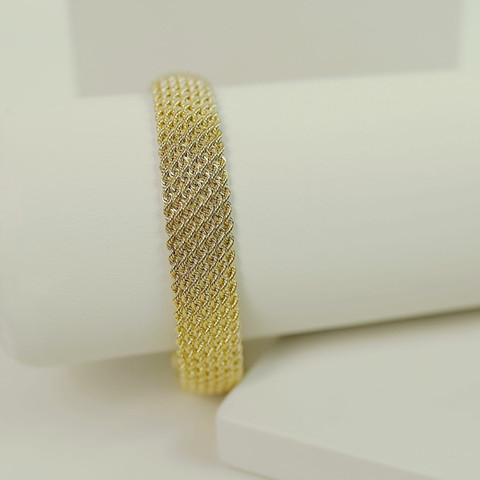 Wide gold mesh (woven) bracelet on a white roll, white studio blocks.