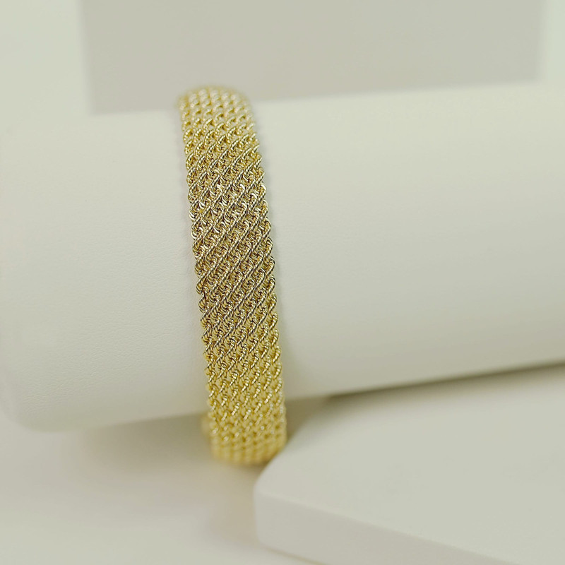 Wide gold mesh (woven) bracelet on a white roll, white studio blocks.