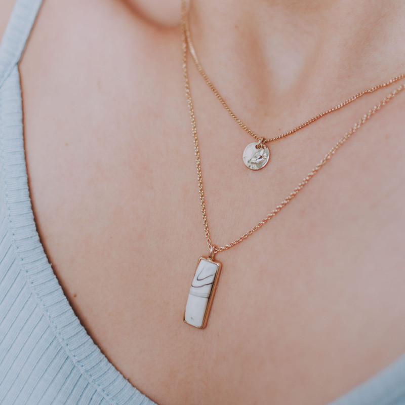 Layered fine gold chains with a disc and a bar pendant on warm skin, pale blue knit.