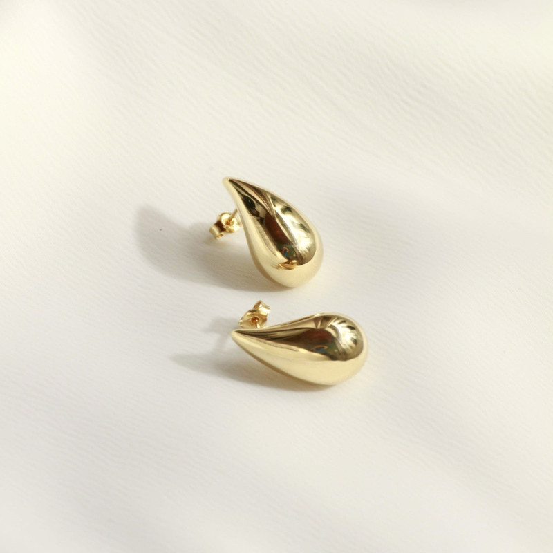 Pair of polished gold teardrop earrings on a white sheet.
