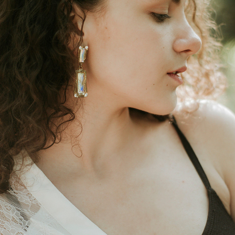 Woman with curly hair in natural light wearing long baguette crystal drop earrings.
