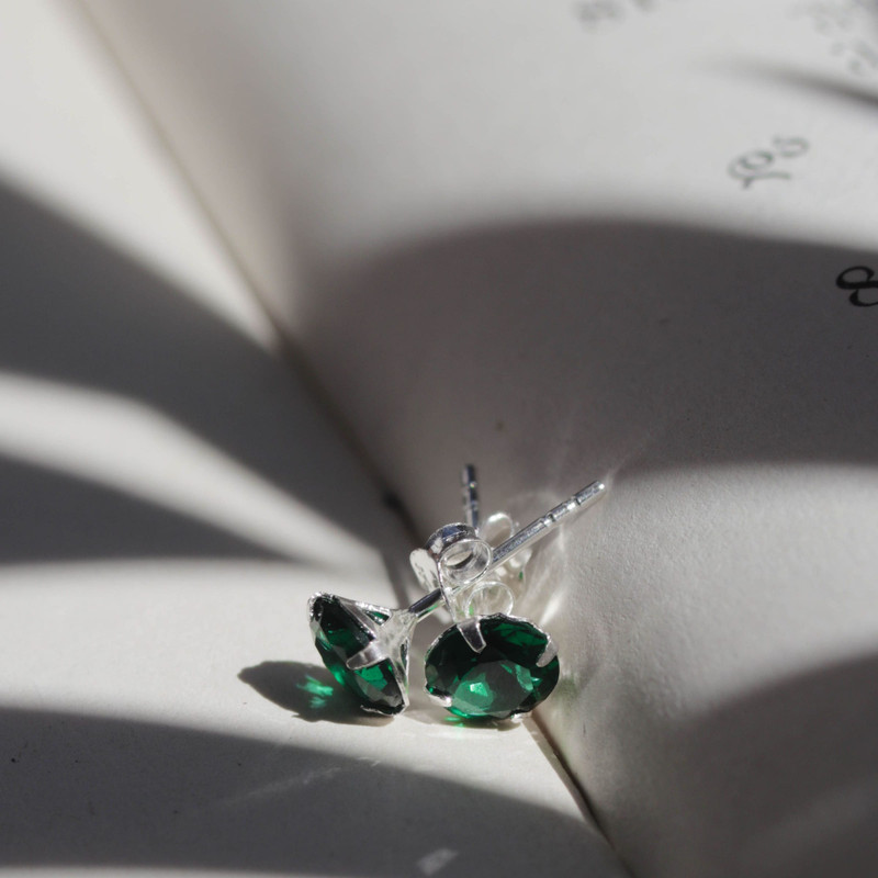 Emerald-and-diamond studs on an open book page with leaf shadows, cool grey light.