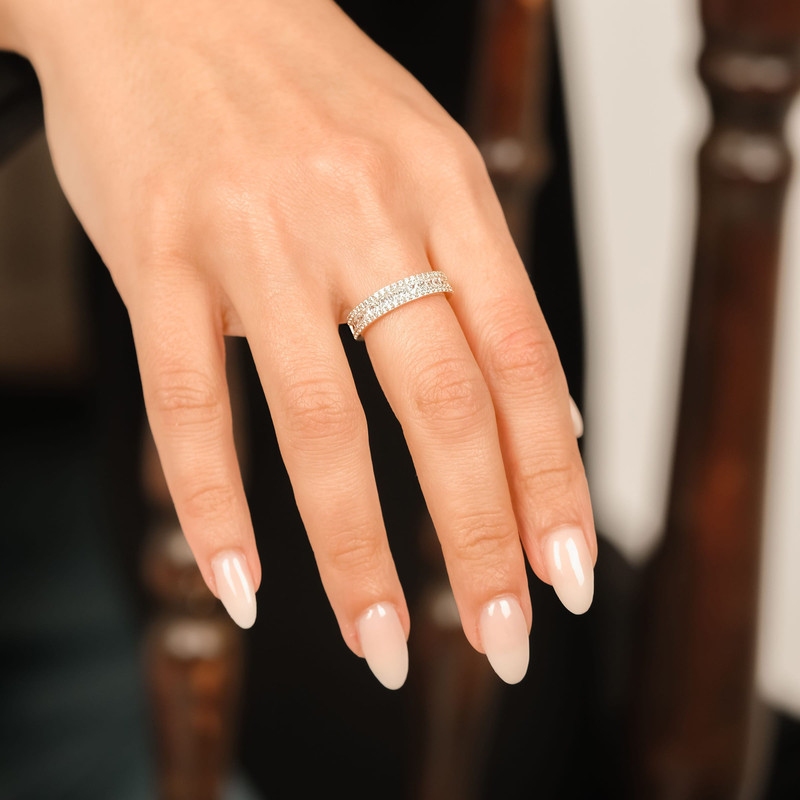 Relaxed hand with a pavé diamond band on the ring finger, warm wood blur behind.