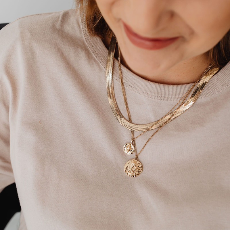 Closer view of the same layered gold chains and coin pendants on a beige tee.