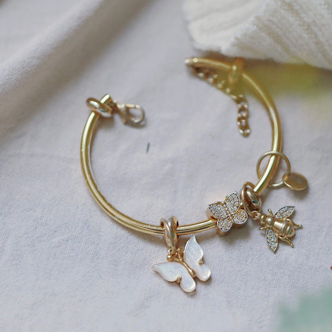 Gold bangle with dangling charms on soft white knit (cropped to exclude a plant).