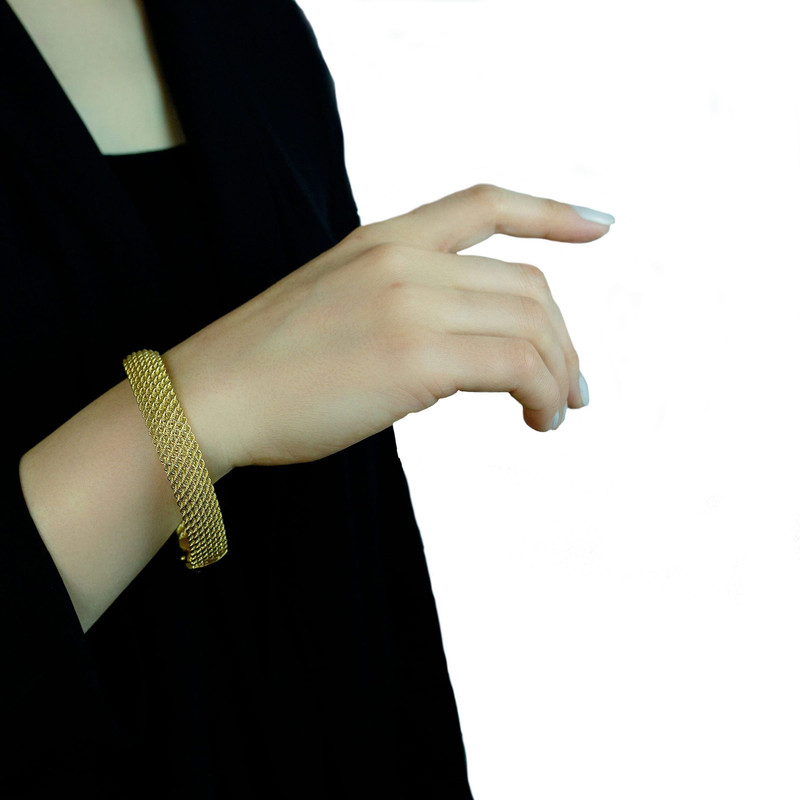 Arm in a black sleeve wearing the same gold mesh bracelet, white background.