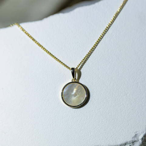 Gold chain with a round milky moonstone pendant against white stone.