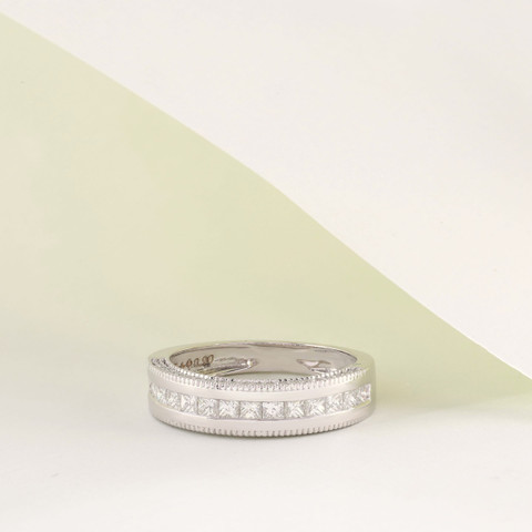 White-metal band with a channel of princess-cut stones between milgrain edges, on white.