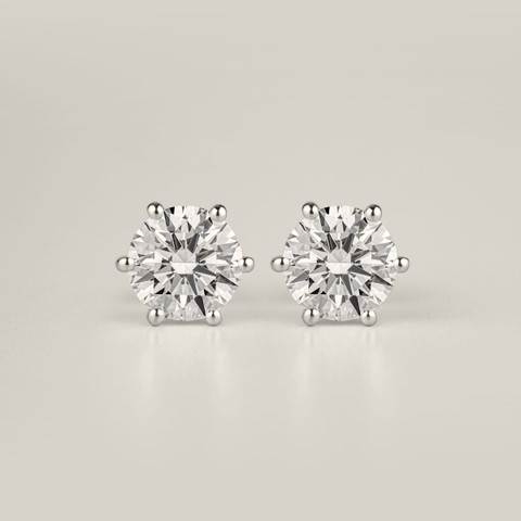 Pair of six-claw round diamond studs in white metal on a pale grey sweep.