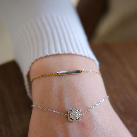 Wrist in a white knit sleeve wearing a fine gold bar bracelet and a diamond charm chain.