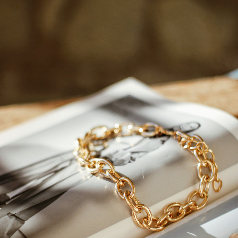 Chunky gold link bracelet laid over a magazine page in warm light.