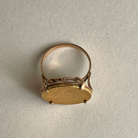 Vintage gold signet ring with an oval face on a warm stone-grey paper surface.