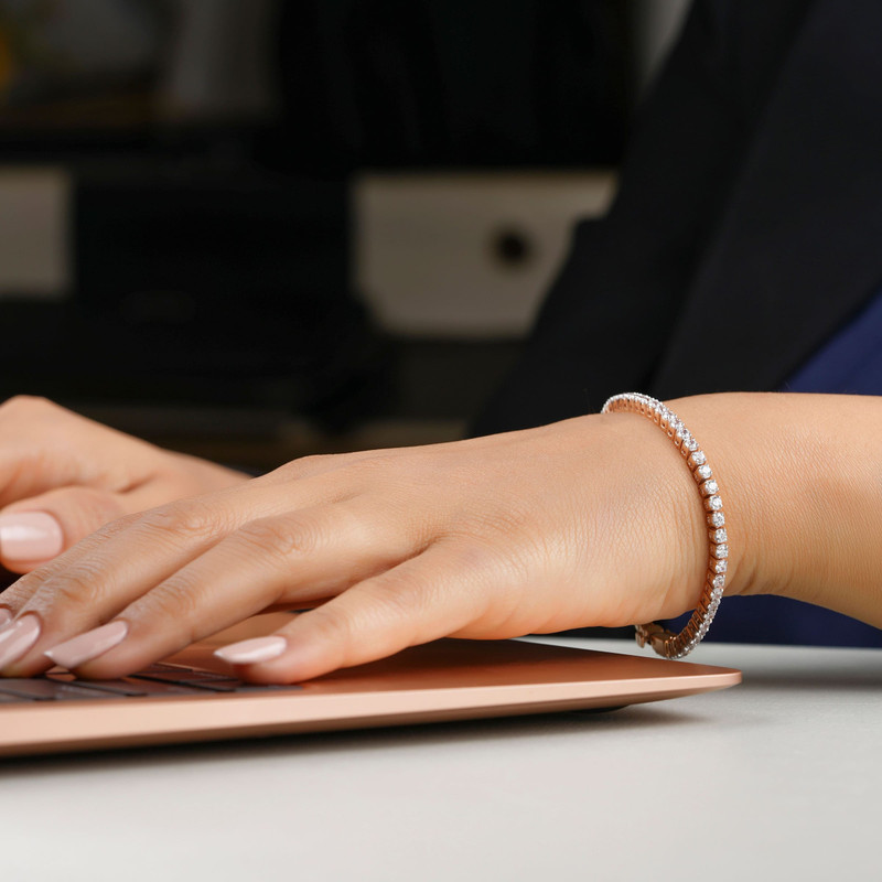Hands typing on a rose-gold laptop wearing a fine diamond tennis bracelet.