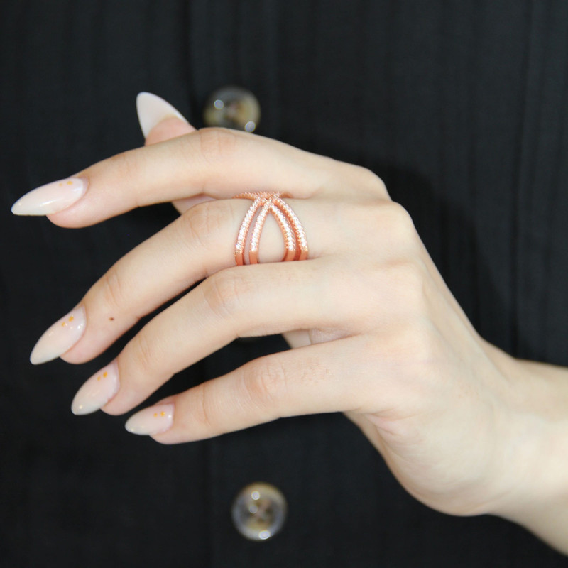 Manicured hand wearing an openwork rose-gold ring against a dark outfit.