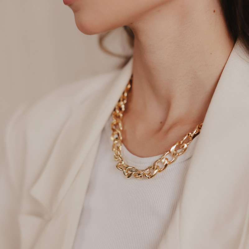 Chunky interlocking gold chain worn with a cream blazer and white top.