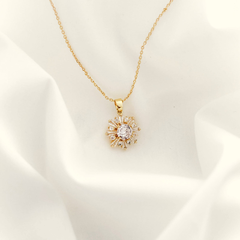 Gold chain with a starburst pendant set with a centre stone, on soft white fabric.