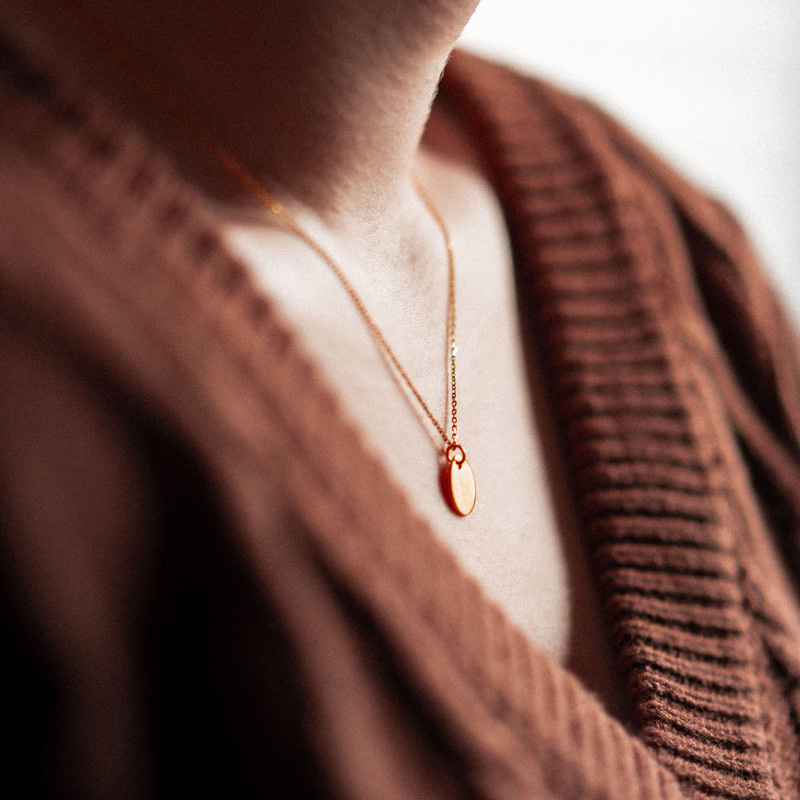 Fine gold chain with a small oval pendant over a rust-brown knit cardigan.
