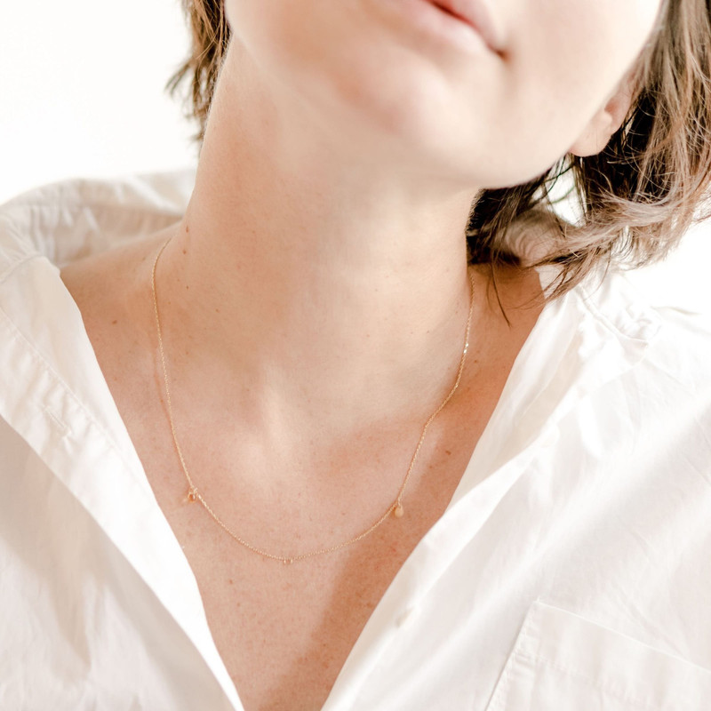 Woman in a white shirt wearing a very fine gold necklace, bright soft light.