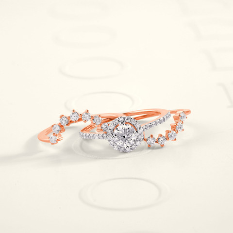 Rose-gold bridal stack: diamond halo engagement ring with two curved pavé bands, on white.