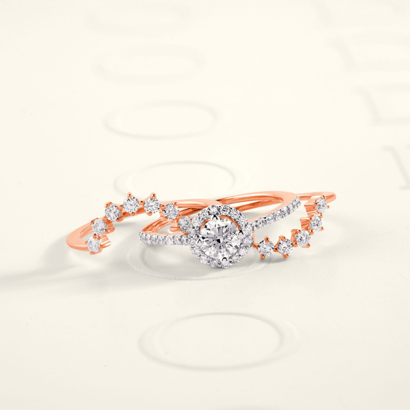 Rose-gold bridal stack: diamond halo engagement ring with two curved pavé bands, on white.