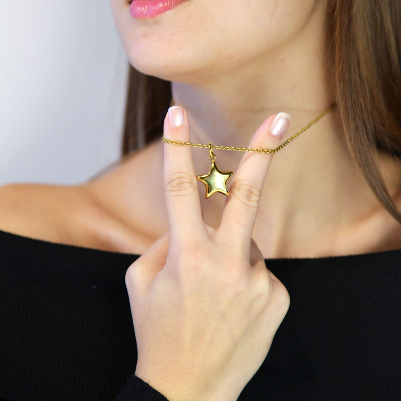 Woman holding a small gold star pendant up to the camera, black off-shoulder top.