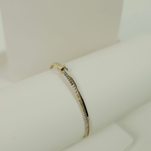 Slim gold bangle with a pavé-set front on a white roll, white studio blocks.