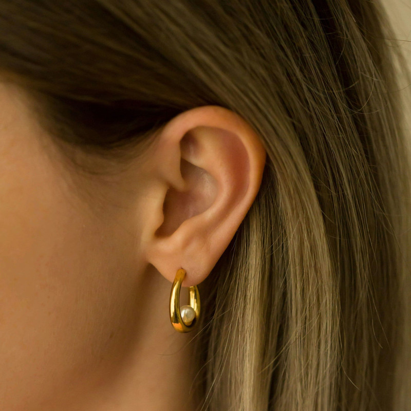 Close crop of an ear wearing a small chunky gold drop huggie, warm blonde hair.