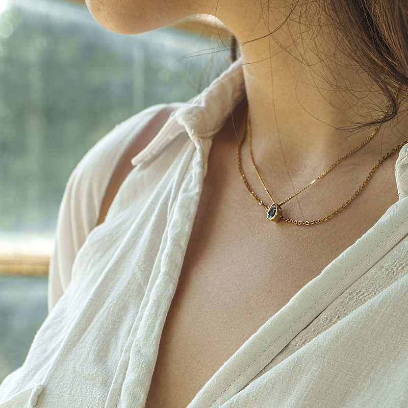 Woman in a cream linen shirt wearing a fine gold necklace with a small drop pendant.
