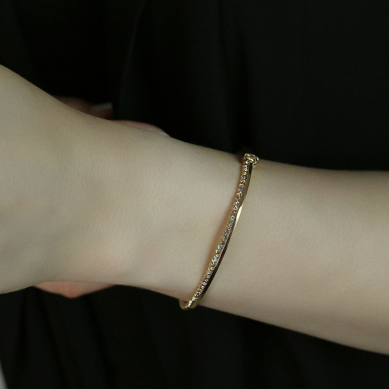 Wrist wearing the same slim pavé gold bangle, dark background.